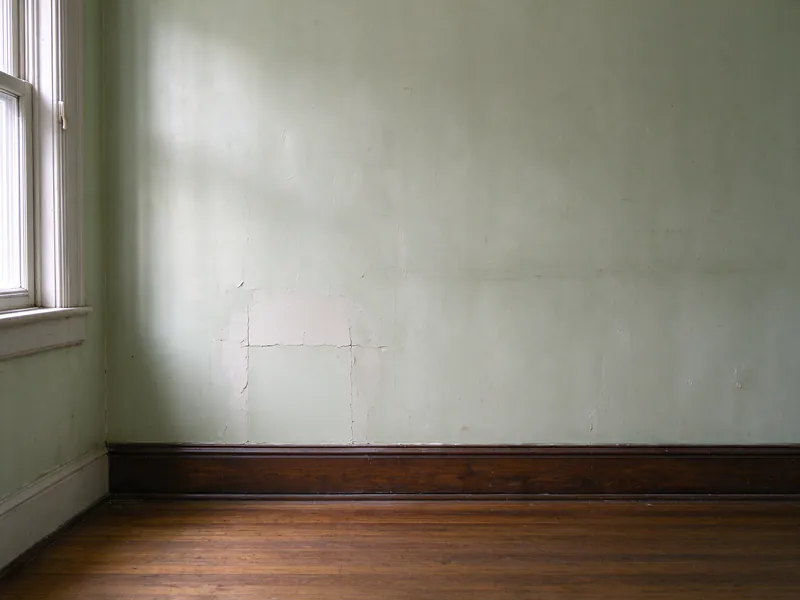 After: the same pale green wall with the opening patched flush with plaster and the baseboard continuous