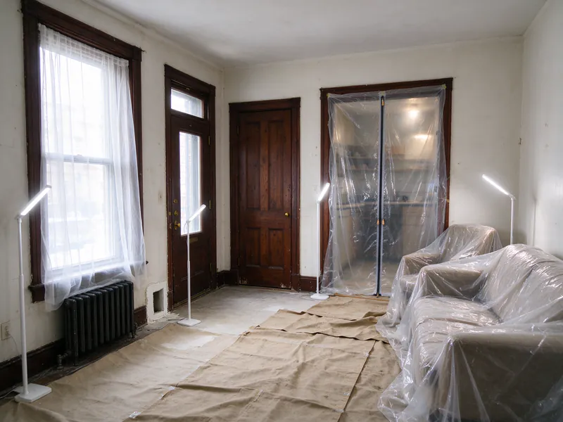 Rowhouse living room with furniture under plastic, drop cloths and a zippered plastic dust barrier over the kitchen doorway
